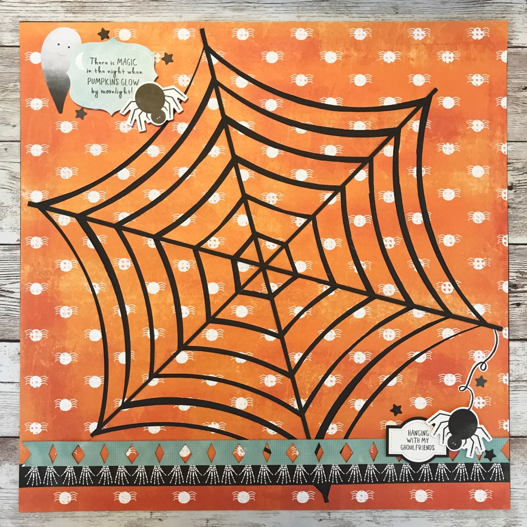 Halloween layout with a large spider web in the background and spider embellishments.