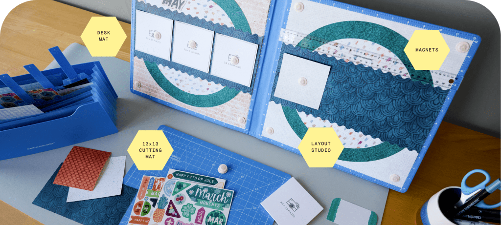 A workspace featuring a desk mat, a 13x13 cutting mat, and a layout studio with magnets, alongside a blue organizer filled with various crafting supplies and stickers.
