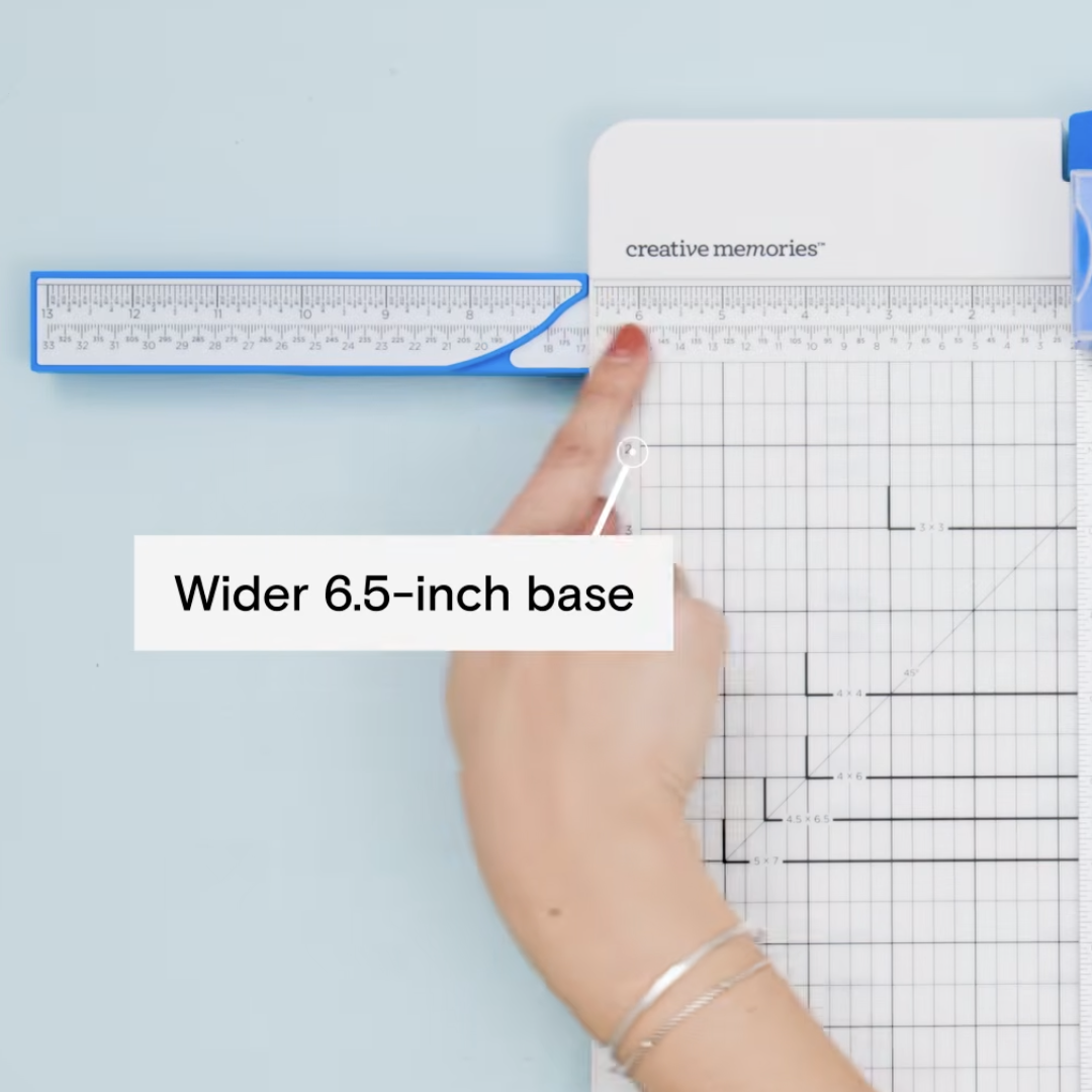 Close-up of a hand pointing to a ruler on a crafting tool with a wider 6.5-inch base, set on a light blue background.